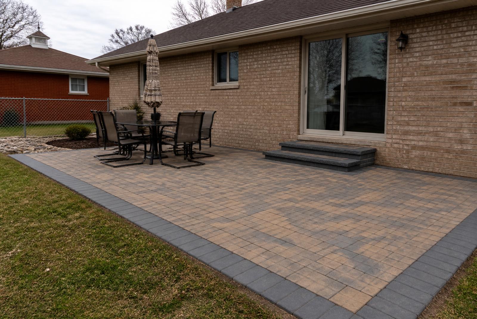 Finished paver patio with a charcoal soldier course border behind a brick Michigan home