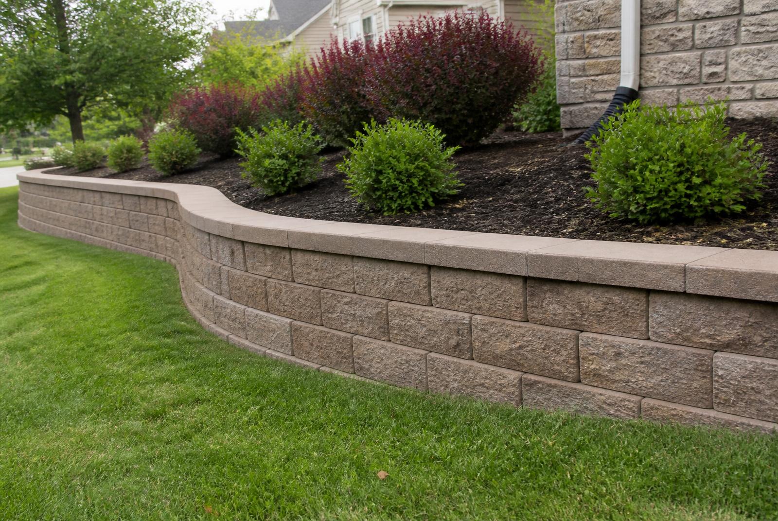 Segmental block retaining wall with capstones holding a planted bed above a lawn